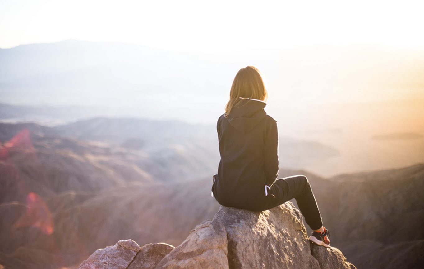 back of woman's head looking out across a mountain scene at sunrise